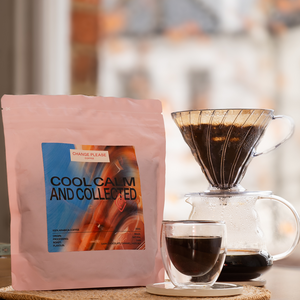 Coffee bag labeled 'Cool Calm and Collected' next to a coffee maker and cup on a blurred background