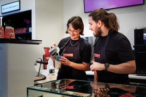 Two baristas in a coffee shop preparing a drink.