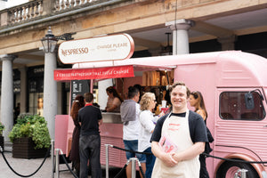 Person in an apron standing in front of a pink Nespresso for Change Please coffee truck.