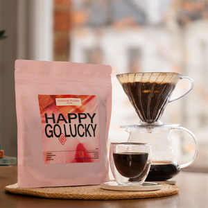 Coffee bag labeled 'Happy Go Lucky' with a coffee cup and filter on a blurred background
